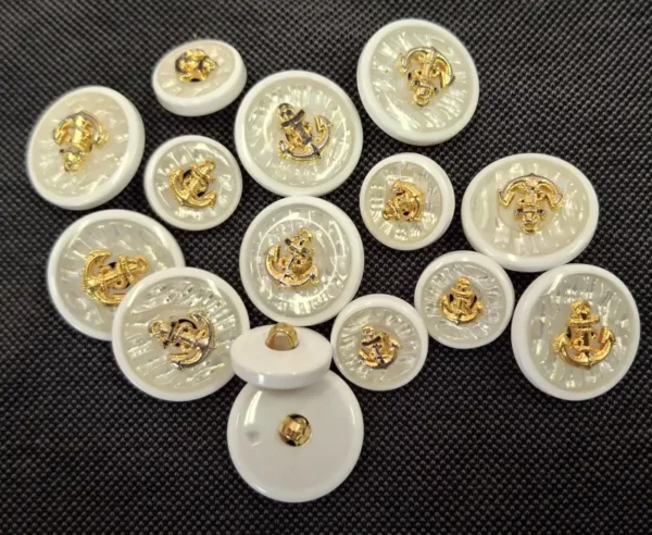 bouton décoratif avec un motif d’ancre dorée sur un fond nacré. L’ancre évoque un thème nautique ou maritime, souvent associé aux uniformes de la marine ou à la mode inspirée des marins. L’association du blanc et de l’or lui donne un aspect élégant et classique.